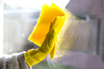 hand in yellow rubber glove holding yellow microfiber cleaning cloth and spray bottle with...