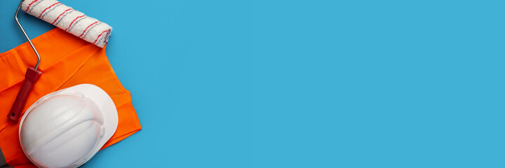 Construction helmet, signal vest and paint roller on a blue background. Banner. Top view, flat lay