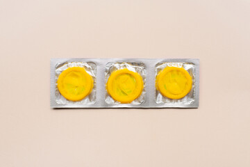Colorful composition with yellow condoms on beige background. Safe sex and contraceptive concept. Flat lay, top view, copy space.