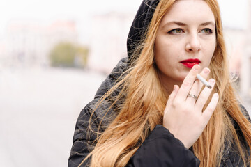 Fototapeta na wymiar Girl with cigarette. Woman smokes outdoors. Closeup portrait. Unhealthy smoking habit