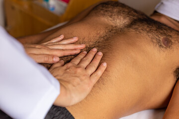 Detalhe de mãos de fisioterapeuta fazendo massagem em barriga de paciente.