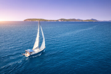 Aerial view of beautiful white sailboat in blue sea at bright sunny summer evening. Adriatic sea in Croatia. Landscape with yacht, mountains, transparent blue water, sky at sunset. Top view of boat - Powered by Adobe