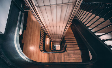 Wide-angle view from the top of a long stairwell going down in a helix in an antique house with a...