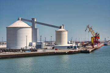 Two industrial silos with harbour cranes in the background at the port of Calais, France