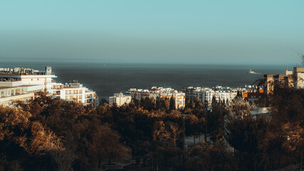 Fototapeta na wymiar An evening cityscape of a dormitory area near the sea with multiple multi-story residential buildings lit by warm sunset light and a park zone in the foreground, Oeiras district of Lisbon, Portugal