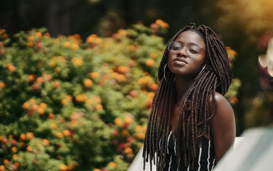 A ravishing young black female with dreadlocks and eyeglasses in the public park with a bush with...