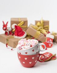 red ceramic cup with cocoa and marshmallows, behind a gift box