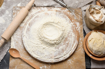 white wheat flour heaped on a round wooden board, kneaded dough with a wooden plate
