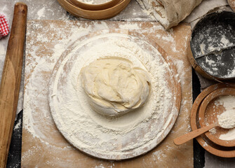 kneaded dough of white wheat flour lies on a round wooden board