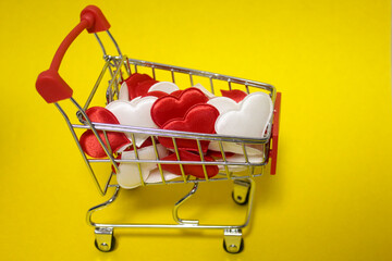 A small supermarket cart that is full of Valentine's Day hearts on a yellow background.