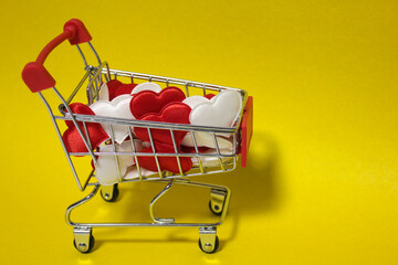 A small supermarket cart that is full of Valentine's Day hearts on a yellow background.