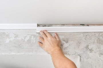 Worker fixes the plastic molding to the ceiling. Installation of ceiling cornice.