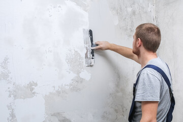 A male worker spreads the putty mixture and flattens the wall.