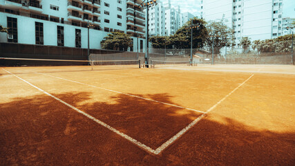Wide-angle view from the corner of an empty outdoor tennis court with an orange clay ground; warm sunny afternoon, Rio de Janeiro, Brazil