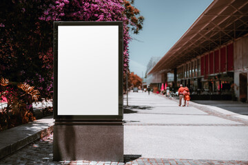 An outdoor mockup of a blank information poster on the sidewalk near a lilac tree; an empty vertical street banner template; billboard placeholder mock-up on a city boulevard on a warm bright day