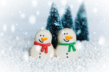 Winter scene with two snowman macaroons, christmas trees and snow
