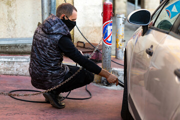  Man shakes a car wheel on the street in service station, automatic pump, auto tire pumping. Car mechanic inflating tire