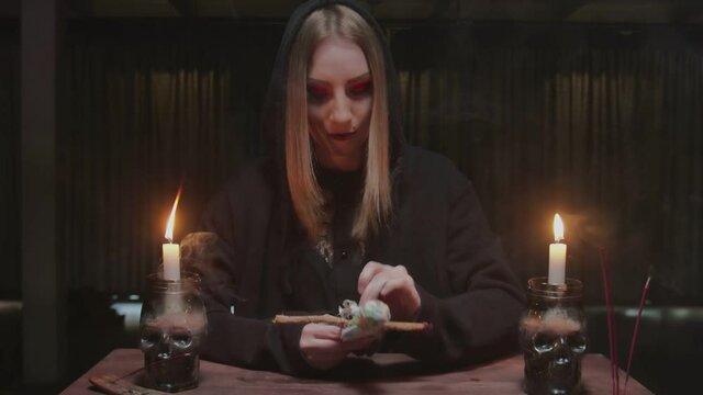 Young witch female fortune teller sticks a needle into voodoo doll in terrible magic ritual