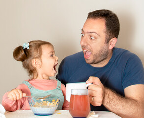 Handsome young father together with cute baby daughter having breakfast together. Dad and child eating corn flakes morning at home during quarantine of pandemic Coronavirus. Happy fathers day concept.