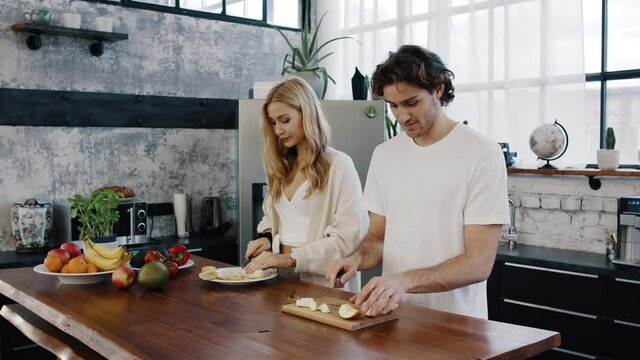 Young attractive couple cuts fruits together and prepare a healthy fruit-bowl, porridge-bowl, acai-bowl in modern kitchen