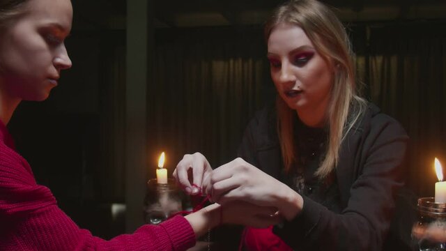 Young witch female fortune teller ties a red rope on client's hand