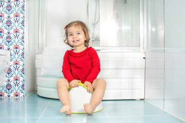 Beautiful smiling little baby sitting on potty in bathroom. Cute adorable funny child girl using chamber pot. Toilet training concept. Toddler learning to use the Toilet.