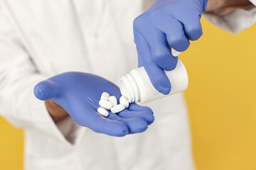 Smiling medical doctor with pills. Isolated over yellow background. Man in a blue gloves.