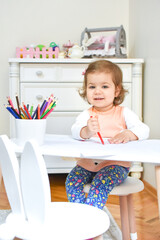 Cute adorable baby girl drawing a picture with colored pencil at home or kindergarten. Toddler child painting on paper. Kid playing in nursery.