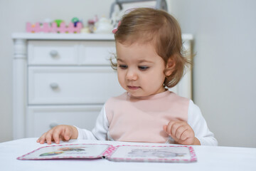 Naklejka premium Cute adorable baby girl reading a book at home or kindergarten. 