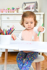 Cute adorable baby girl drawing a picture with colored pencil at home or kindergarten. Toddler child painting on paper. Kid playing in nursery.