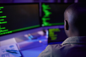 Unrecognizable African American soft developer sitting at desk in front of computers working on new code, rear view shot