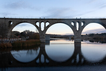 Cobblestone rail bridge and its reflection on the lake river