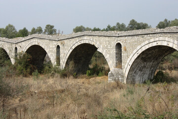 Ura e Terzive or Terzijski Bridge, also known as Tailors' Bridge, an Ottoman stone bridge near Gjakova in Kosovo, with arches over dry grass