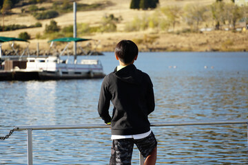 Fototapeta premium Young sporty Asian boy looking at the view on a wood pier at the Lake. Teenager concept