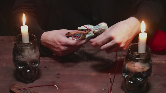 Close up of mysterious wizard male fortune teller uses voodoo doll and red rope to terrible magic ritual