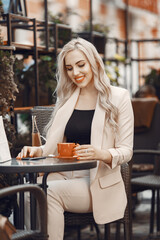 Lady drinks a coffee. Woman sitting at the table. Blonde in a white suit.