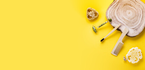 Eco beauty concept. Jade face roller, loofah sponges, toothbrush, wooden comb, wood slice on yellow...