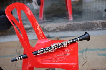 Black wooden clarinet instrument placed on red plastic chair, selectable focus.