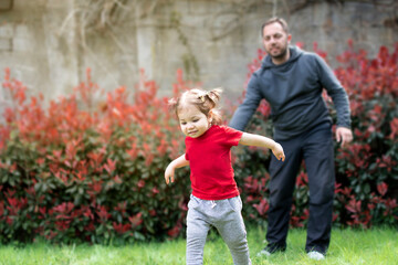 Happy family having fun together on a green lawn in the park. Cute adorable little baby girl playing with her father in garden. Dad spend time with toddler child outdoors. Happy father's day concept.