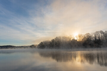 Fototapeta na wymiar Fog rises on the water of Lake Lanier in Georgia at sunrise under a blue and orange sky