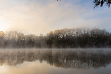 Fog rises on the water at sunrise on Lake Lanier in Georgia with a reflection of trees in the water in winter