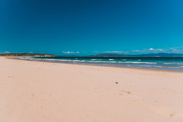 pristine wild landscape at Clifton Beach in Tasmania, Australia with wavy blue ocean and golden sand next to a rugged coastline
