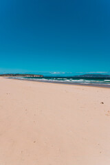 pristine wild landscape at Clifton Beach in Tasmania, Australia with wavy blue ocean and golden sand next to a rugged coastline