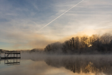 Fog on the surface of the water at sunrise with a blue and orange sky on Lake Lanier outside of Atlanta, Georgia with a dock