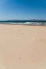 pristine wild landscape at Clifton Beach in Tasmania, Australia with wavy blue ocean and golden sand next to a rugged coastline