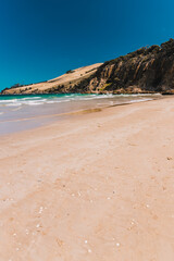 pristine wild landscape at Clifton Beach in Tasmania, Australia with wavy blue ocean and golden sand next to a rugged coastline