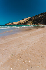 pristine wild landscape at Clifton Beach in Tasmania, Australia with wavy blue ocean and golden sand next to a rugged coastline
