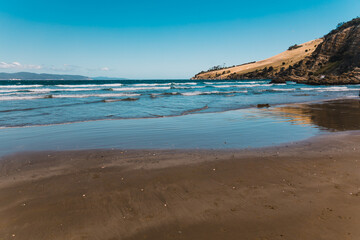 pristine wild landscape at Clifton Beach in Tasmania, Australia with wavy blue ocean and golden sand next to a rugged coastline