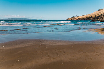 pristine wild landscape at Clifton Beach in Tasmania, Australia with wavy blue ocean and golden sand next to a rugged coastline