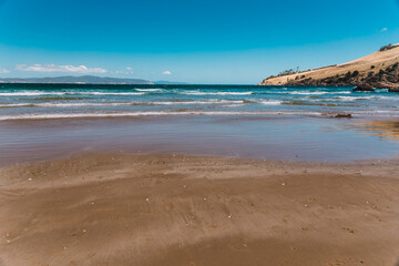 pristine wild landscape at Clifton Beach in Tasmania, Australia with wavy blue ocean and golden sand next to a rugged coastline
